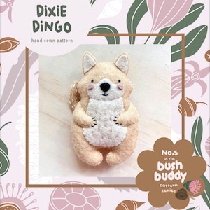 Może przedstawiać: Ręcznie szyty wzór z filcu dla uroczego, beżowego Dingo, zwanego Dixie Dingo. Jest częścią serii wzorów "Bush Buddy", nr 5. Wzór umieszczono na tle różowych i zielonych ilustracji kwiatowych.