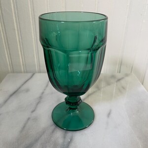 May include: A deep emerald green glass goblet featuring a faceted, multi-sided bowl design. The drinking vessel has a thick, sturdy stem with a hexagonal base detail and a wide, circular foot, providing a stable foundation for the glass.