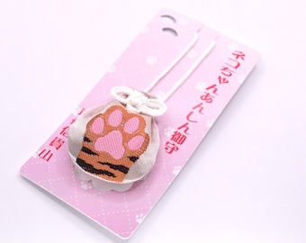 Könnte beinhalten: Ein kleiner, beigefarbener Stoffbeutel mit einer gestickten rosa Katzenpfote und braunen, tigerartigen Streifen. Der Beutel hat eine weiße Kordel, die oben zu einem dekorativen Knoten gebunden ist, und ist auf einer hellrosa Karte befestigt.