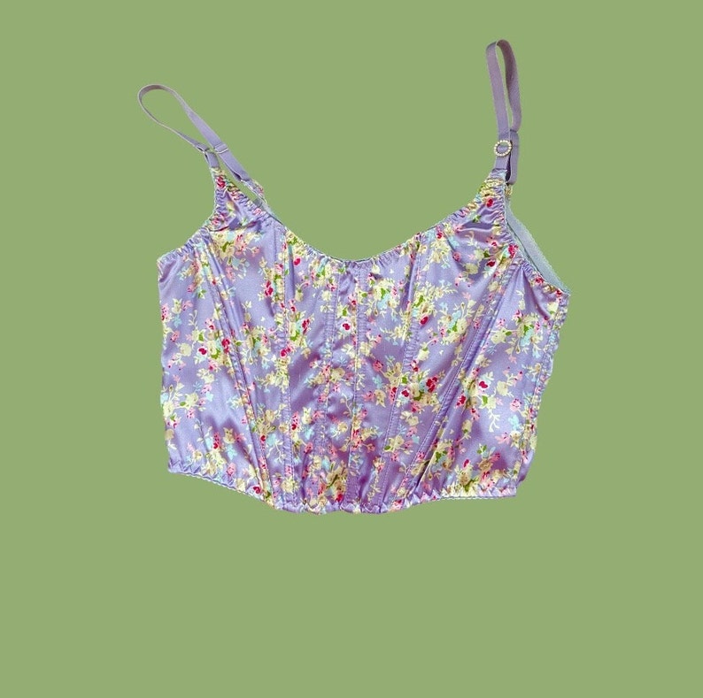 Pode incluir: Um corpete de cetim roxo com estampa floral. O corpete tem al&ccedil;as ajust&aacute;veis e um corpete com barbatanas.