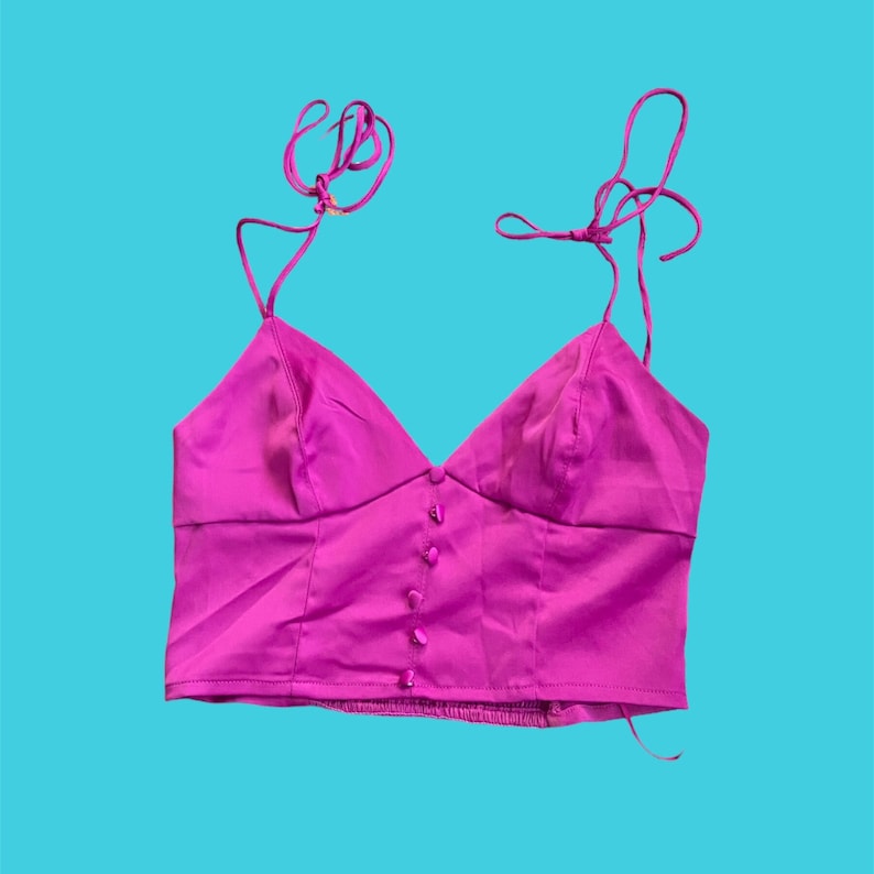 May include: A magenta satin crop top with adjustable straps and a button closure down the front.