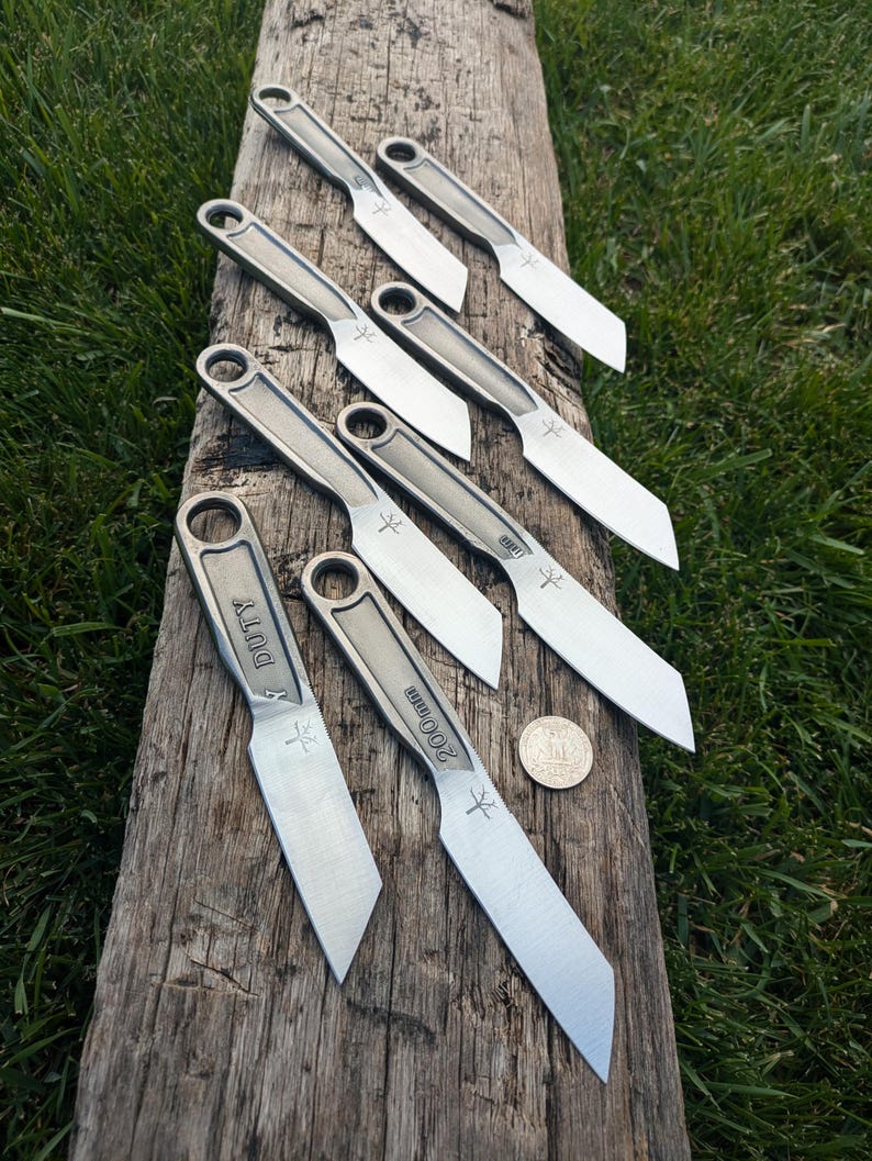 K&ouml;nnte beinhalten: Acht kleine, silberfarbene Messer mit schwarzen Griffen sind auf einer Holzoberfl&auml;che aufgereiht. Die Messer haben unterschiedliche Markierungen auf den Griffen, darunter "S DUTY" und "2000mm". Eine Silberm&uuml;nze ist in der unteren rechten Ecke des Bildes zu sehen.