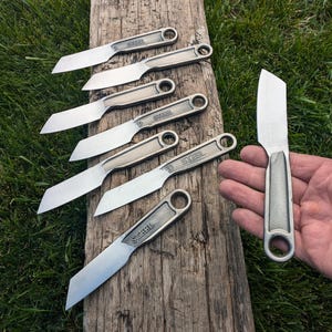 K&ouml;nnte beinhalten: Sechs kleine Messer aus wiederverwendeten Schraubenschl&uuml;sseln mit dem Wort "STEEL" auf dem Griff. Die Messer liegen auf einer Holzoberfl&auml;che. Ein gr&ouml;&szlig;eres Messer aus einem Schraubenschl&uuml;ssel wird in einer Hand gehalten.