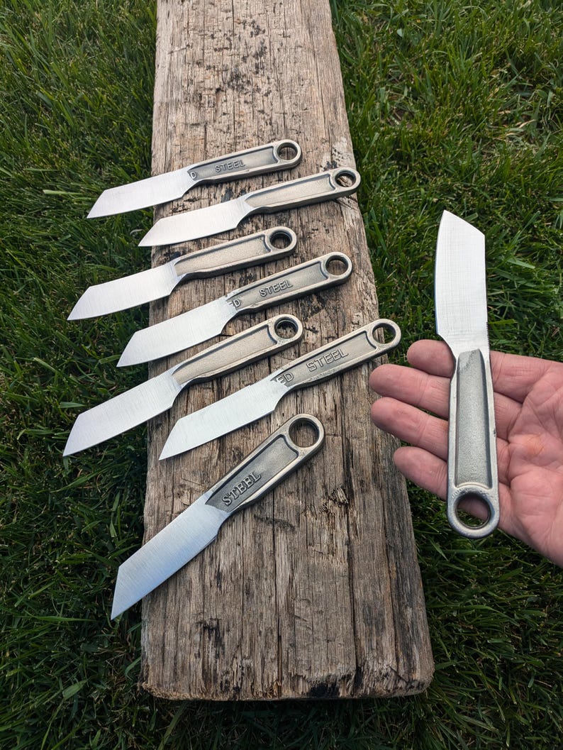 K&ouml;nnte beinhalten: Sechs kleine Messer aus wiederverwendeten Schraubenschl&uuml;sseln mit dem Wort "STEEL" auf dem Griff. Die Messer liegen auf einer Holzoberfl&auml;che. Ein gr&ouml;&szlig;eres Messer aus einem Schraubenschl&uuml;ssel wird in einer Hand gehalten.