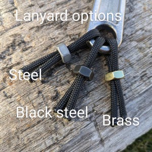 K&ouml;nnte beinhalten: Lanyard-Optionen f&uuml;r einen Schraubenschl&uuml;ssel, gezeigt mit drei verschiedenen Perlenfarben: Stahl, Schwarzstahl und Messing. Der Text "Lanyard options" ist im Bild sichtbar.
