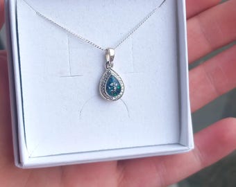 May include: A silver necklace with a teardrop-shaped pendant featuring a green and blue opal stone surrounded by smaller clear stones.