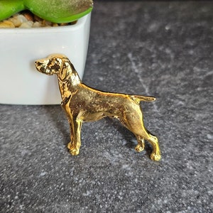 Könnte beinhalten: Eine goldfarbene Metallstift in Form eines Deutsch Kurzhaar Hundes.