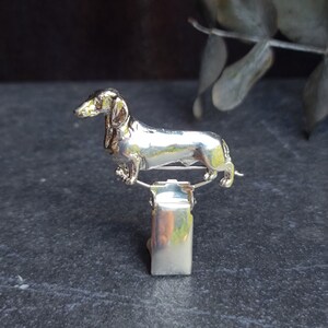 May include: Silver dachshund dog figurine attached to a silver clip.