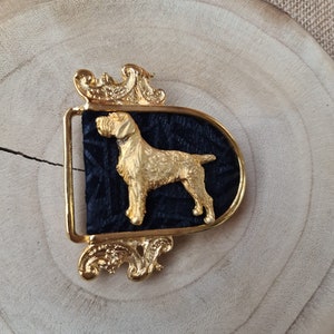 May include: Gold-tone belt buckle with a black velvet background featuring a detailed silhouette of a hunting dog.