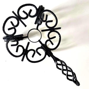 May include: Black wrought iron candle holder with a decorative floral design. The candle holder has a circular centre and a twisted handle. The overall design is ornate and elegant.