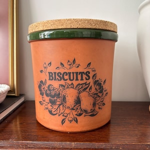 May include: A white ceramic mug with a black handle and the text "But First, Coffee" in a handwritten style. The mug is on a white surface. The mug is approximately 10 cm tall.
