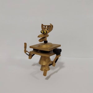 May include: A gold-colored 3D printed robot with a bird-like head and articulated arms. The robot has a square base and a round body.