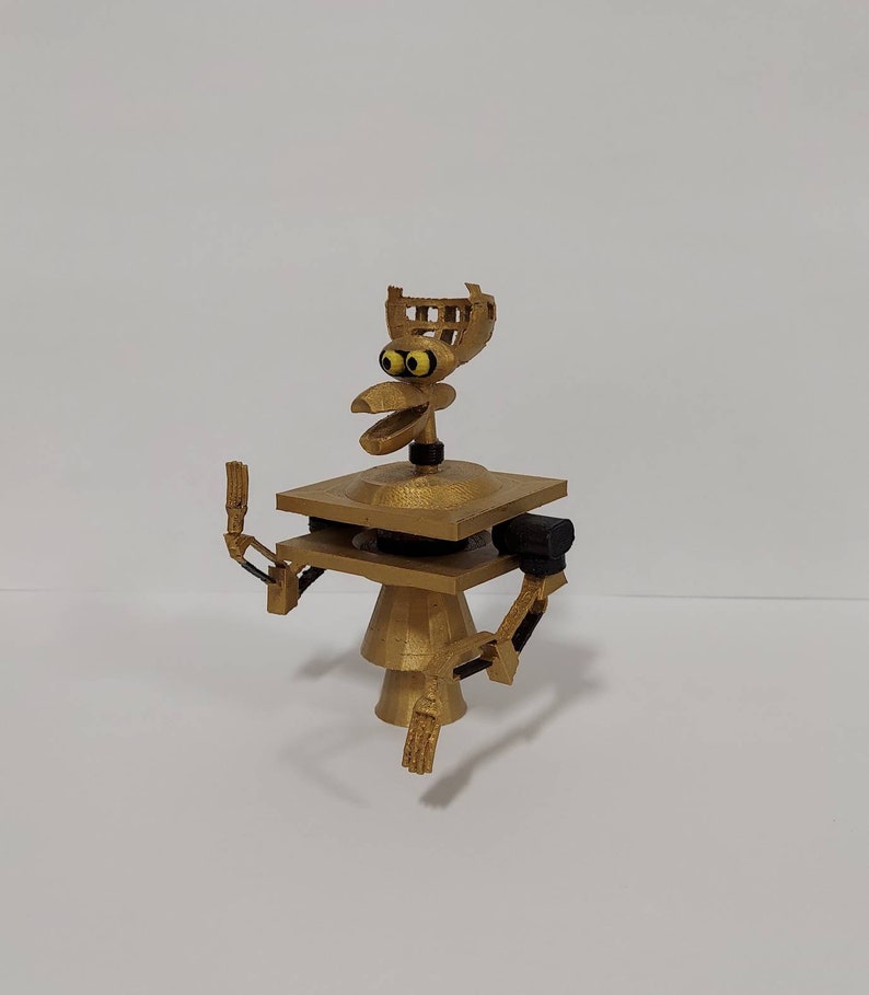 May include: A gold-colored 3D printed robot with a bird-like head and articulated arms. The robot has a square base and a round body.