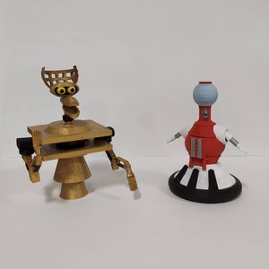 May include: Two robot figurines, one gold with a round base and a square platform, the other red with a white base and a round top.