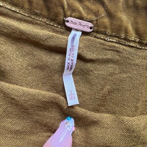 Op de afbeelding: Een bruine fluwelen rok van Free People met een label waarop staat "Made in India" en "Fabrique en Inde". Het label toont ook maat 2 UK 6.