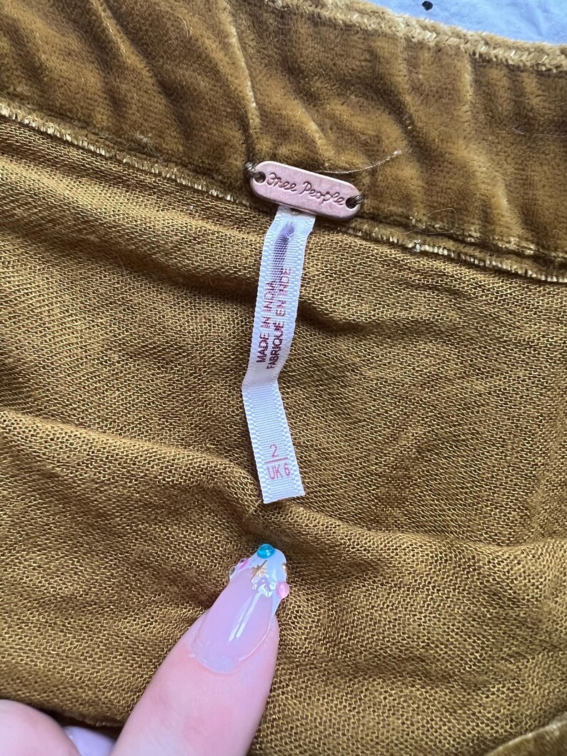 Op de afbeelding: Een bruine fluwelen rok van Free People met een label waarop staat "Made in India" en "Fabrique en Inde". Het label toont ook maat 2 UK 6.