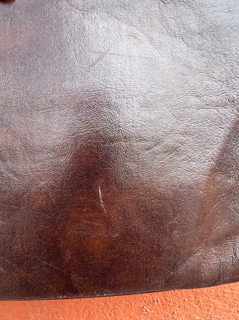 May include: Close-up of a brown leather surface with a smooth, shiny finish. The leather has a subtle texture and a few light scratches.