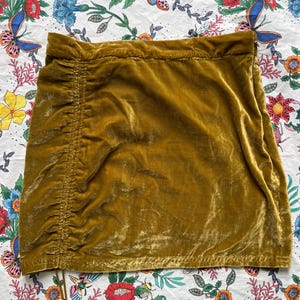 Op de afbeelding: Een mosterdgele mini-rok van fluweel met een trekkoord in de taille en een geplooide zijkant.