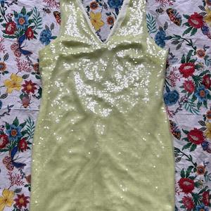 Puede incluir: Un vestido sin mangas de color verde claro con lentejuelas y escote en V.