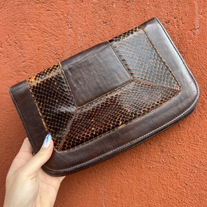 May include: A brown leather clutch with a snakeskin pattern. The clutch has a flap closure and a geometric design.