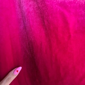 Puede incluir: Primer plano de una vibrante tela fucsia con textura sutil y pliegues. El degradado de color cambia de un tono m&aacute;s oscuro a uno m&aacute;s brillante. Se ve una u&ntilde;a rosa con un peque&ntilde;o coraz&oacute;n rojo.