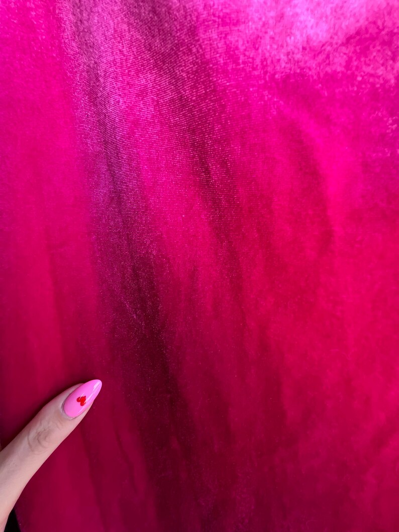 Puede incluir: Primer plano de una vibrante tela fucsia con textura sutil y pliegues. El degradado de color cambia de un tono m&aacute;s oscuro a uno m&aacute;s brillante. Se ve una u&ntilde;a rosa con un peque&ntilde;o coraz&oacute;n rojo.