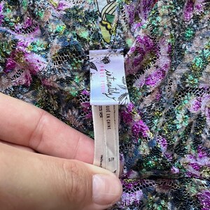 May include: Close-up of a floral patterned garment with a V-neck. The fabric is a mix of purple, green, and gold. A tag reads "intimately FREE PEOPLE" and "QUE EN CHINE". The garment is size S/P.