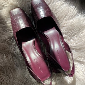 May include: A pair of burgundy faux leather heeled shoes with a crocodile print. The shoes have a slingback strap and the brand name "Charles & Keith" is printed on the insole.