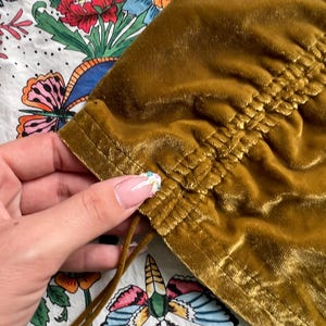 Op de afbeelding: Een mosterdgeel fluwelen top met een trekkoord aan de onderkant. De top heeft een geplooide detail aan de onderkant.