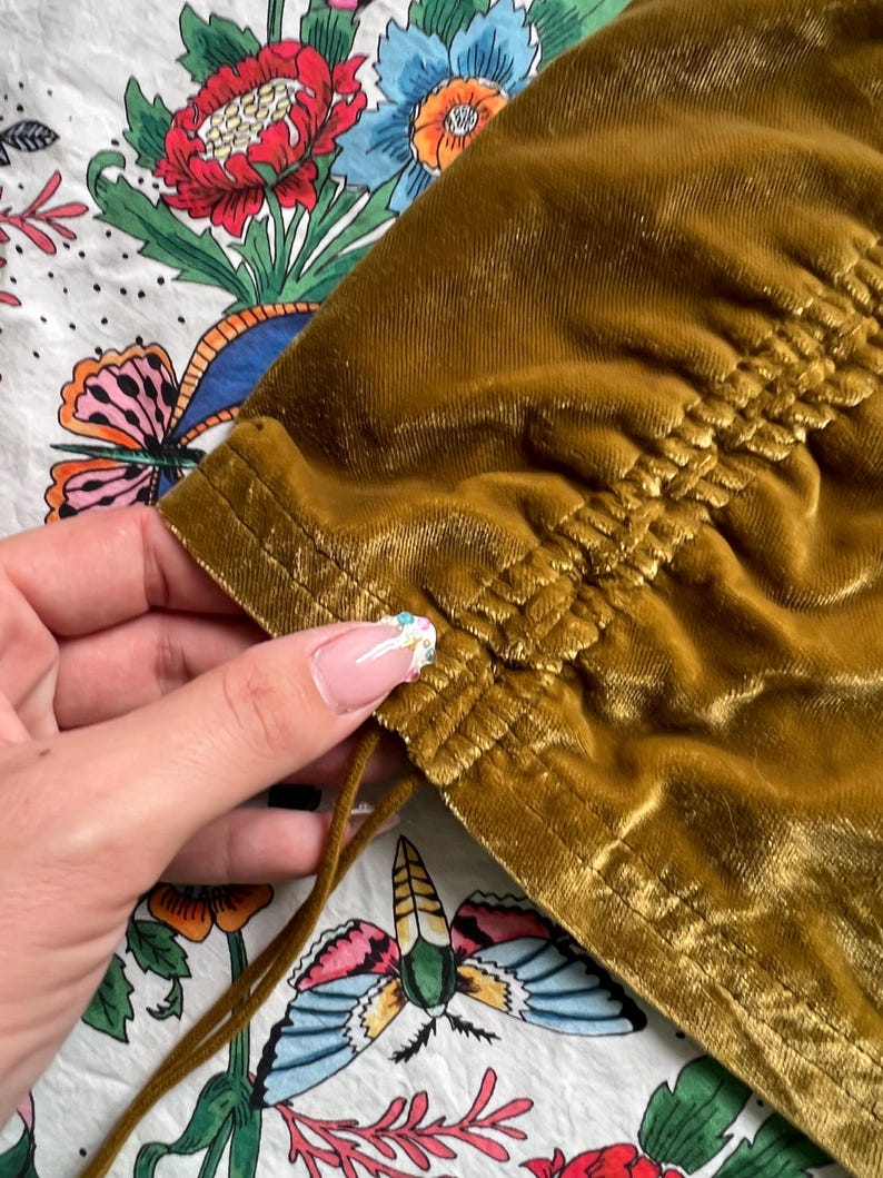 Op de afbeelding: Een mosterdgeel fluwelen top met een trekkoord aan de onderkant. De top heeft een geplooide detail aan de onderkant.