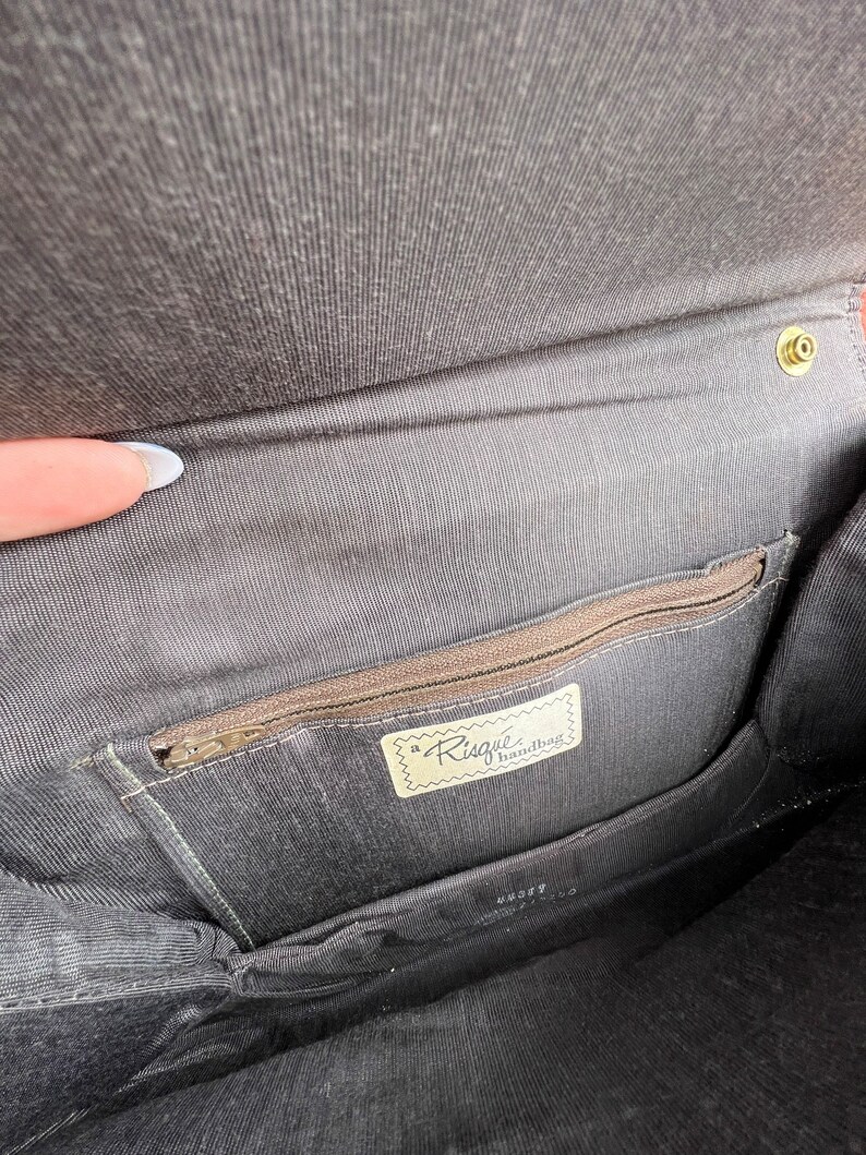 May include: The inside of a black handbag with a zipped pocket and a label that reads "a Risque handbag".