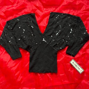 Puede incluir: Top negro con lentejuelas, cuello en V y mangas largas. El top tiene una etiqueta que dice "SUNBOW 2".