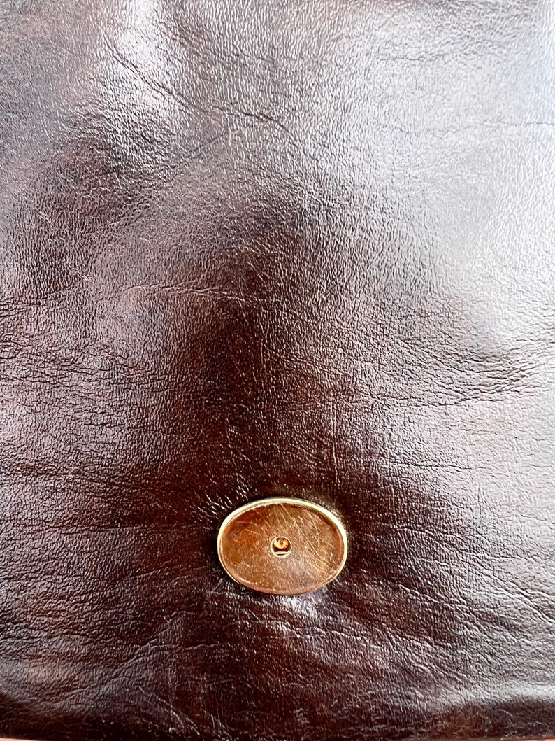 May include: Close-up of a brown leather surface with a gold-coloured metal button.