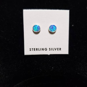 May include: A pair of sterling silver stud earrings with blue opal stones. The earrings are displayed on a white card with the text "STERLING SILVER".