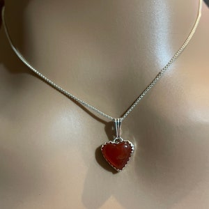 May include: A silver chain necklace with a heart-shaped pendant featuring a red carnelian stone.