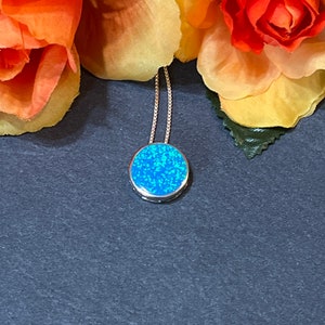May include: A silver chain necklace with a round blue opal pendant. The pendant is set in a silver bezel.