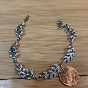 May include: A silver bracelet with white opal leaves. The bracelet is about the size of a US penny.