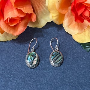 May include: A pair of silver earrings with oval-shaped abalone shell inlays. The earrings have a braided design around the edge of the inlay.