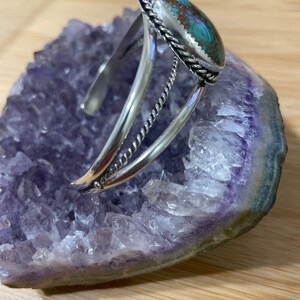 May include: A silver bracelet featuring a turquoise stone set in a silver bezel. The bracelet has a twisted wire design and is open on one side.