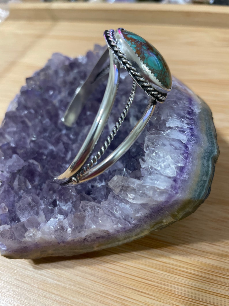 May include: A silver bracelet featuring a turquoise stone set in a silver bezel. The bracelet has a twisted wire design and is open on one side.