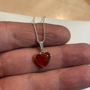 May include: A silver chain necklace with a heart-shaped pendant featuring a red carnelian stone.