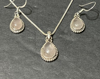 May include: A silver necklace and earrings set with a teardrop-shaped pink stone pendant and matching earrings.