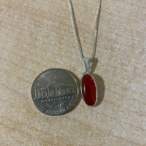 May include: A silver chain necklace with a red carnelian gemstone pendant. The pendant is oval shaped and has a silver setting.