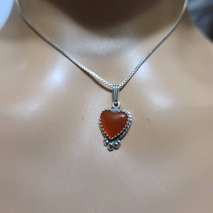 May include: A silver chain necklace with a heart-shaped pendant featuring an orange gemstone.