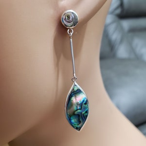 May include: A pair of silver dangle earrings with a round abalone shell at the top and a teardrop-shaped abalone shell at the bottom.