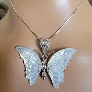 May include: A silver butterfly pendant necklace. The pendant features a mother-of-pearl butterfly with detailed wings. The necklace chain is a delicate silver box chain. The butterfly pendant is approximately 2 inches wide.