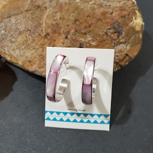 May include: A pair of sterling silver hoop earrings with pink and white abalone shell inlay. The earrings are displayed on a white card with the text "Sterling Silver".