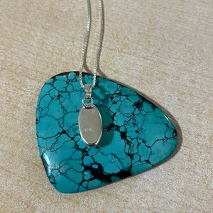 May include: A silver chain necklace with a small oval pendant. The pendant is marked with the number "925" on the back.