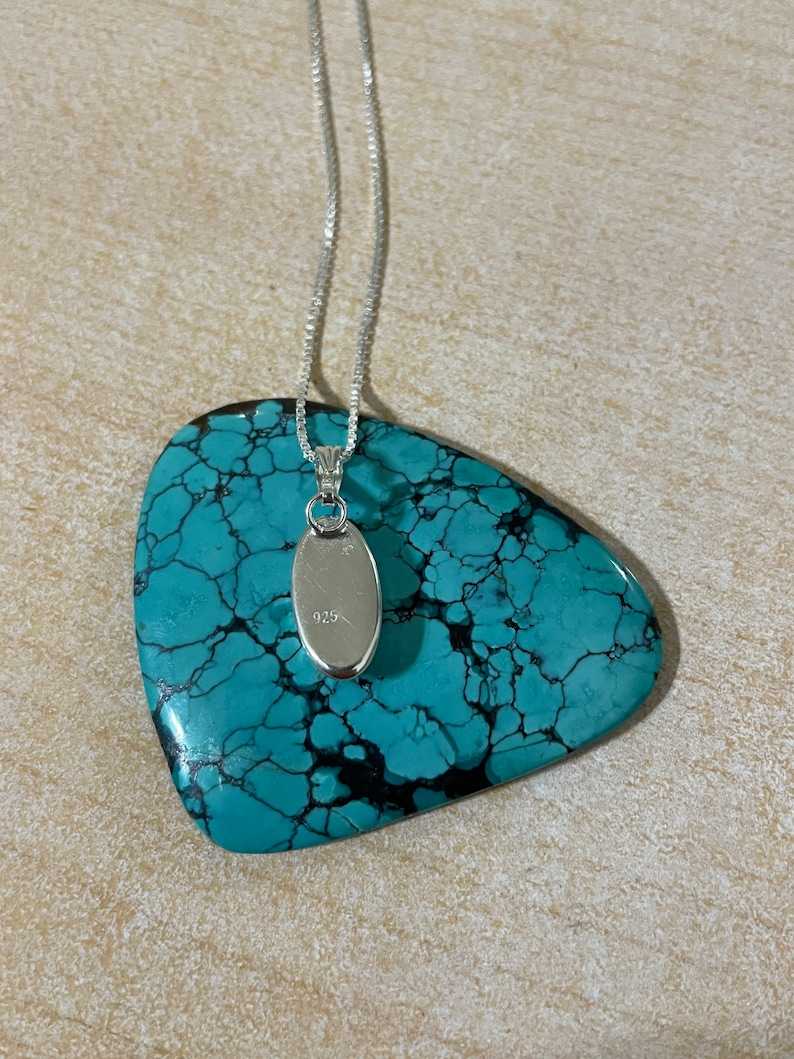 May include: A silver chain necklace with a small oval pendant. The pendant is marked with the number "925" on the back.