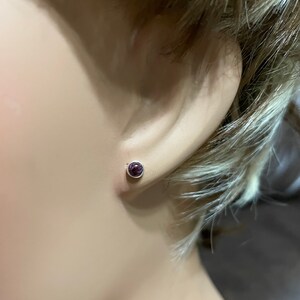 May include: A pair of silver stud earrings with a small, round, purple gemstone in the center.